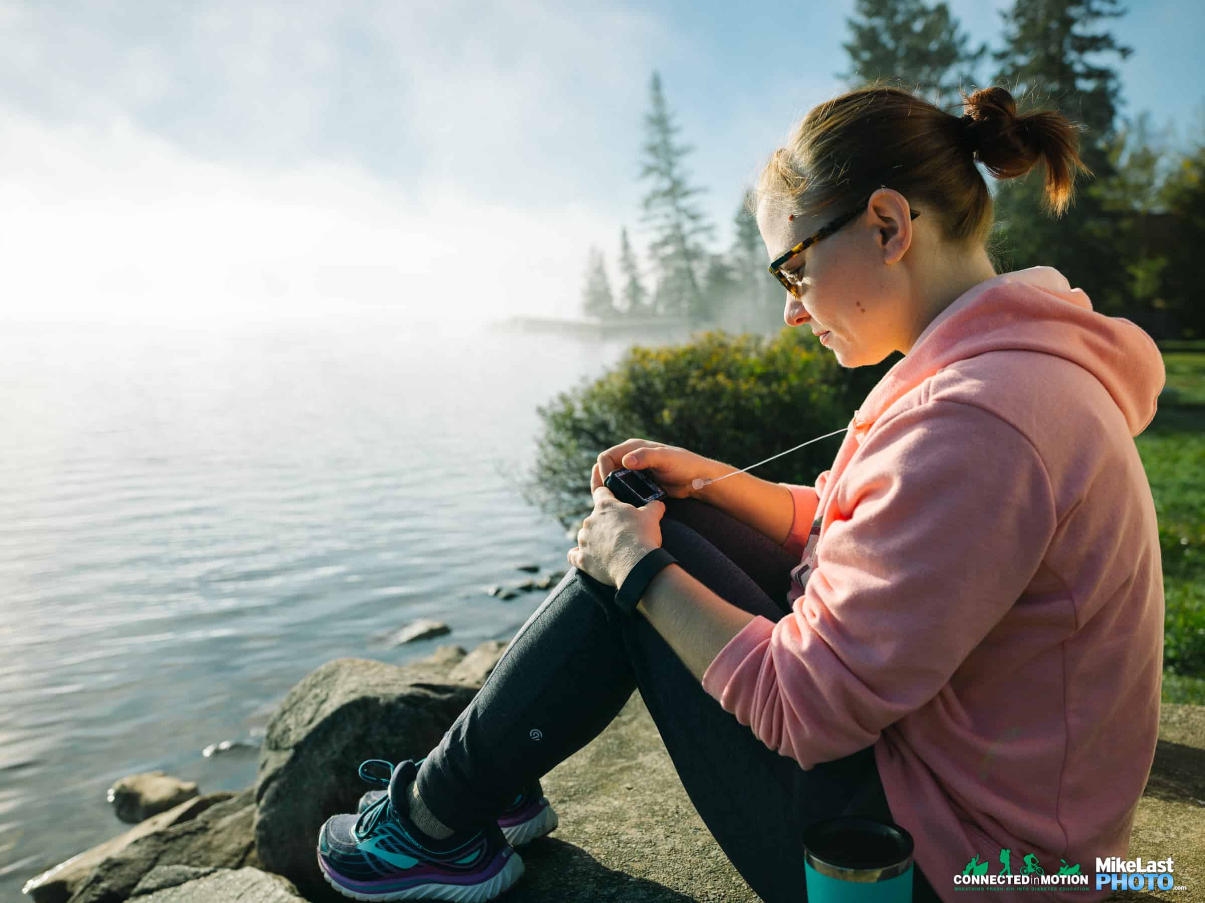 Woman is sitting beside a lake using a Tandem t:slim Insulin Pump.