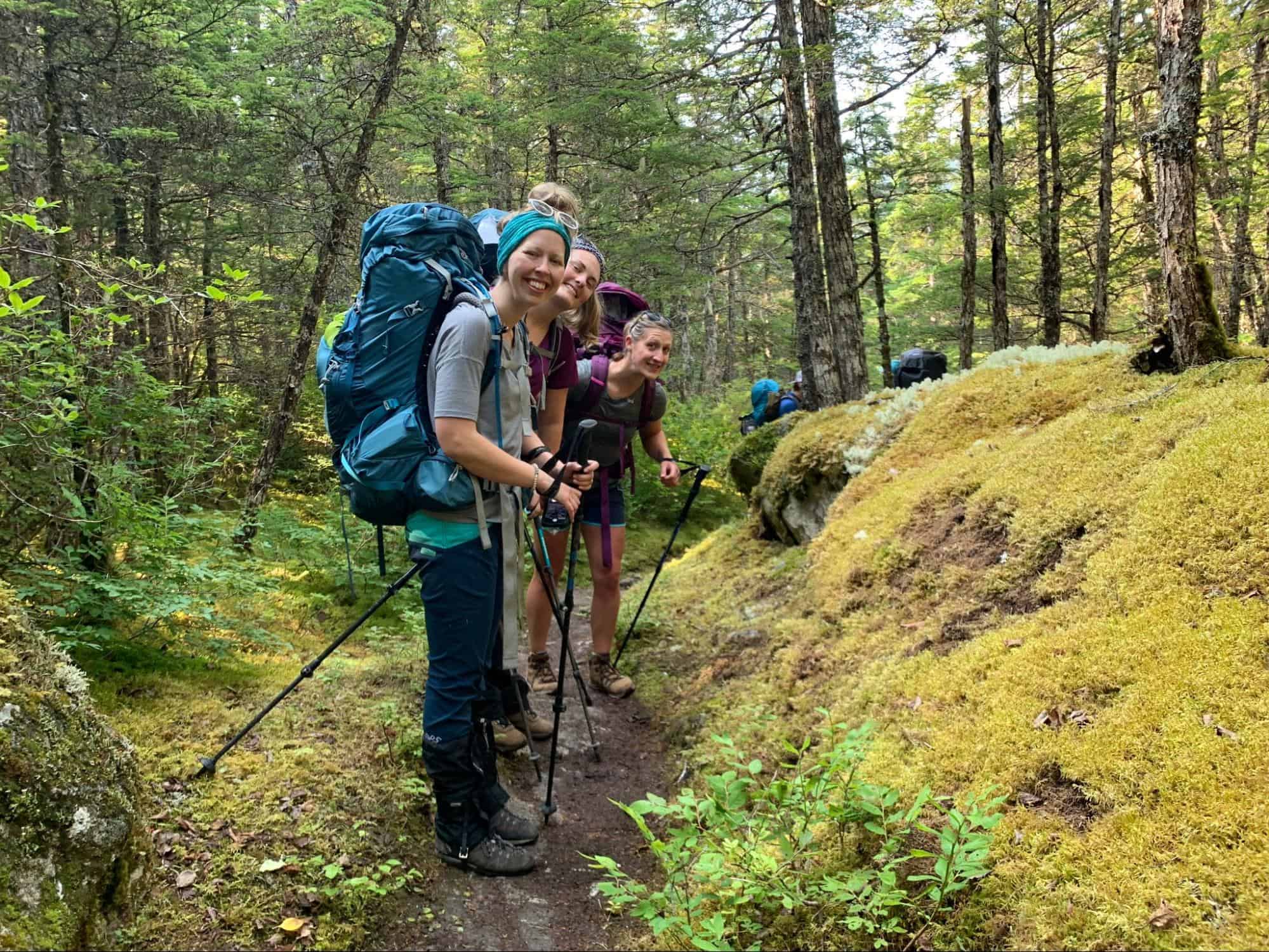 3 backpackers standing in a line on a trail and smiling back at the camera
